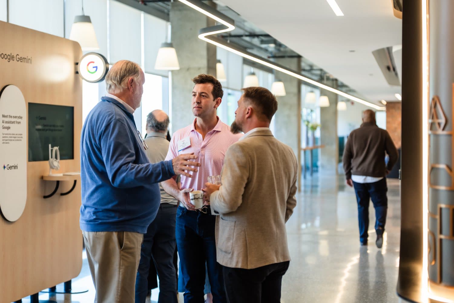 Three attendees talk over drinks beside an interactive technology display.
