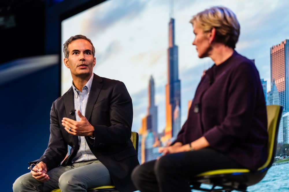 A speaker gestures during a seated conversation onstage, event photography by Jorge Amaya