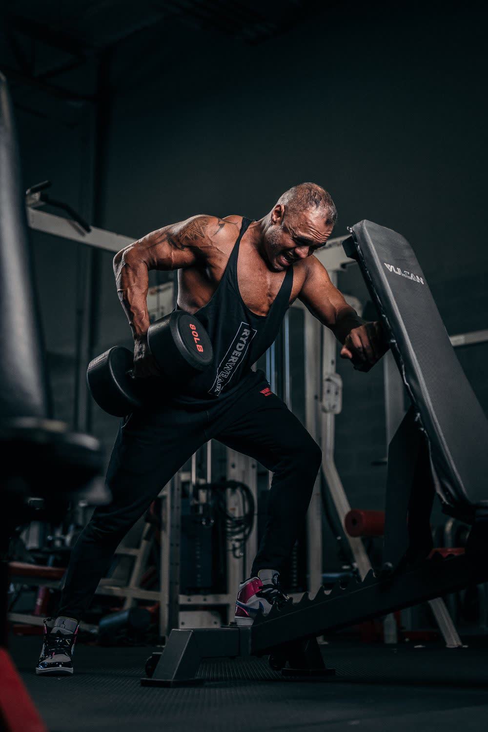 Athlete performing a one-arm dumbbell row beside an incline bench in a gym