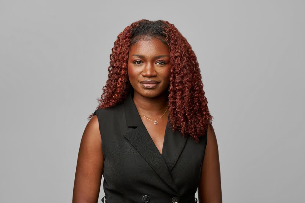 Professional wearing a black sleeveless blazer against a neutral gray backdrop