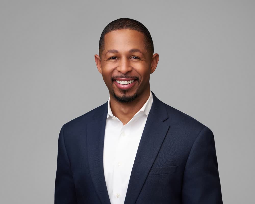 Smiling professional in a navy suit and white shirt against a grey studio background