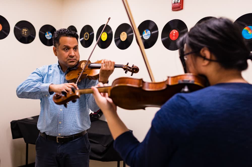 A violin instructor demonstrates technique for a student, lifestyle brand photography by Jorge Amaya