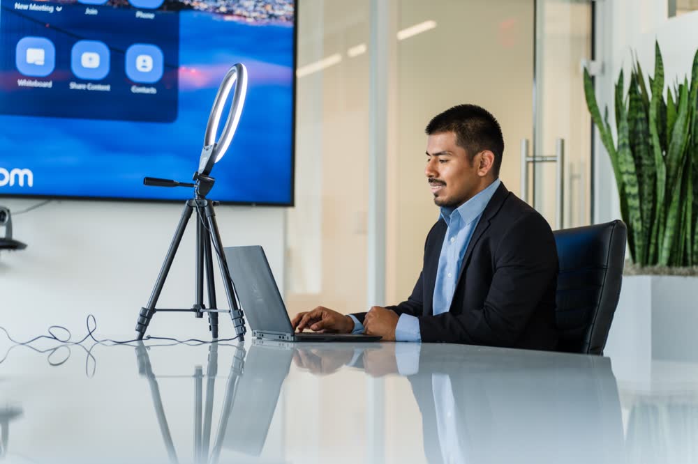 A professional works on a laptop beside a ring light in a modern conference room, on location in Washington DC