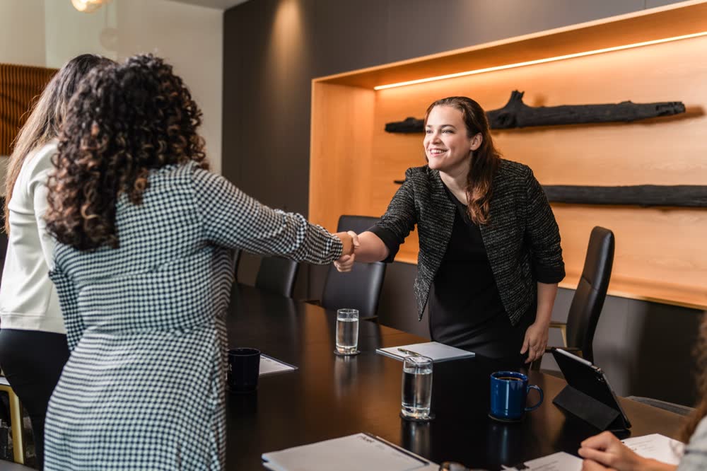 Two professionals shaking hands across a conference table after a meeting