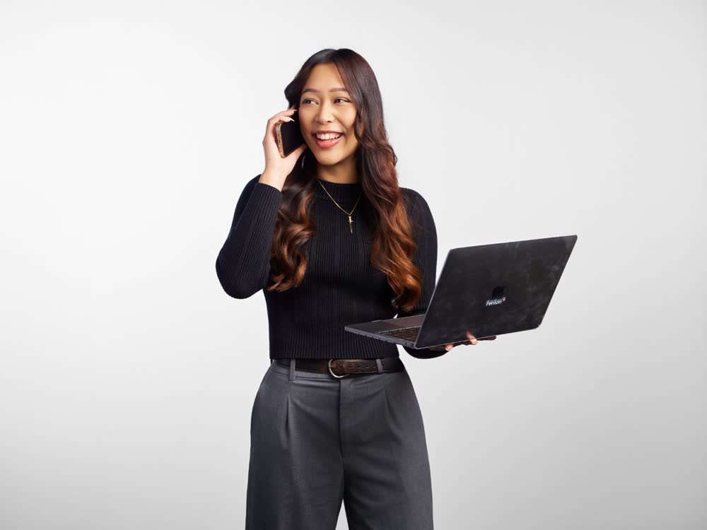 Smiling professional talking on a phone while holding an open laptop against a white studio background