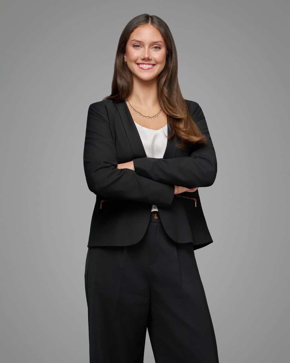 Smiling professional in a dark suit standing with arms crossed against a gray studio background