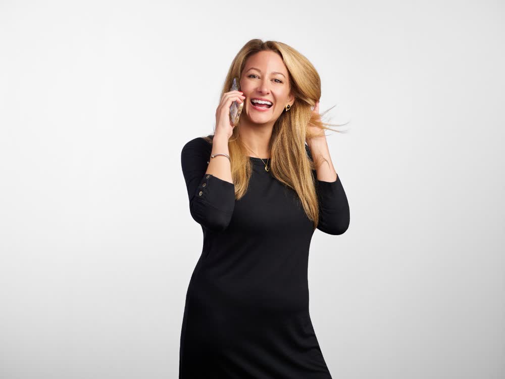 Laughing professional talking on a phone and adjusting their hair against a white studio background